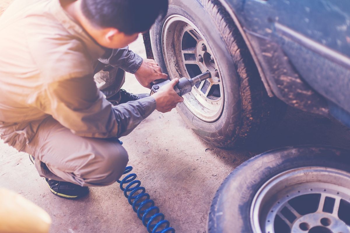 Mechanic changing a car tire in a workshop using an electric drill